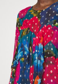 Pestrobarevná hedvábná blůza s květinovým vzorem, na které jsou velké růžové, modré a modrozelené květiny, zdobené lesklými stříbrnými puntíky.