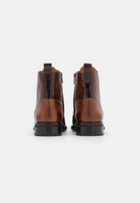 Pár hnědých kožených kotníkových bot s texturovaným vzorem, s zipy na stranách a černými blokovými podpatky, zobrazený ze zadní strany na bílém pozadí.