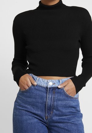 Top court noir à côtes avec un col haut et des manches longues, associé à un jean en denim bleu clair taille haute avec fermeture à bouton.