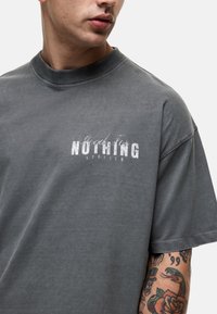 Grijze oversized t-shirt gemaakt van zachte katoen, met een vervaagde grafische druk "Good For NOTHING" in het wit op de borst en een klassieke ronde hals.