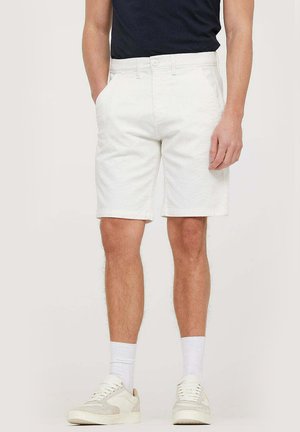Shorts en coton blanc avec une coupe droite, poches avant et passants de ceinture, associés à des baskets blanches et des chaussettes blanches mi-mollet.