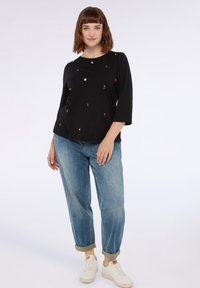 Camiseta negra de manga corta con detalles de bordado multicolor, combinada con jeans cortos de color azul claro y zapatillas blancas.