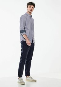 Světle šedá košile na knoflíky s tmavě modrým manžetou, námořnické kalhoty a béžové tenisky. Košile má jemný kostkovaný vzor a rovný střih.