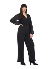 Czarny kombinezon z fasonem kopertowym, przezroczystymi długimi rękawami, związanym w talii i szerokimi nogawkami. Gładka faktura i jednolity kolor.