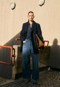Wijde blauwe jeans, donkerblauw dubbelgebreefd coat en een bruin handtas. Gladde texturen met een op maat gemaakt ontwerp en contrasterende kleuren.