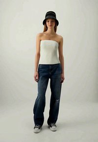 Top strapless à côtes blanches associé à un jean large déchiré bleu et un chapeau seau noir. Des baskets noir et blanc complètent le look.