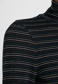 Col roulé noir avec des rayures horizontales en turquoise, blanc et fils métalliques multicolores. Texture douce avec un détail subtil d'épaules bouffantes.