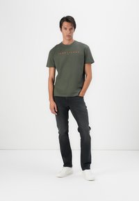 Groene katoenen T-shirt met het "TOMMY JEANS" logo in oranje. Gecombineerd met donkere denim jeans en witte sneakers. Eenvoudige, casual pasvorm.