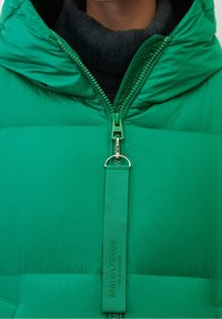 Grøn pufferjakke med høj krave, fuld lynlås og logomærke. Glat tekstur, polstret design med sølv lynlås træk og accent syning.