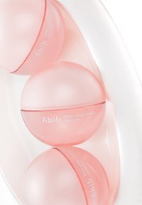Trois contenants sphériques translucides roses étiquetés « Abib PDRN collagen lip mask Glazed jelly » disposés sur une surface blanche lisse.