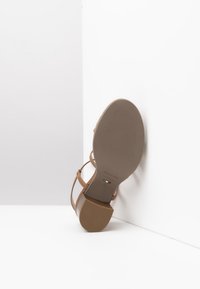 Beige Riemchensandale mit niedrigem, strukturiertem Absatz. Die Sohle trägt ein Markenlabel. Glattes Material mit einem minimalistischen Design.