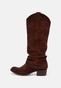 Bottine de cowboy en suédine marron clair, avec un petit talon bloc et des tirettes, vue de côté sur fond blanc.