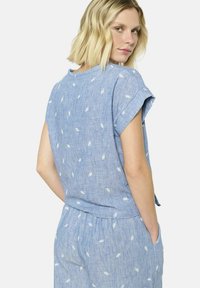 Top de chambray azul claro con mangas cortas enrolladas, que presenta patrones de hojas blancas, ajuste relajado y escote redondo.