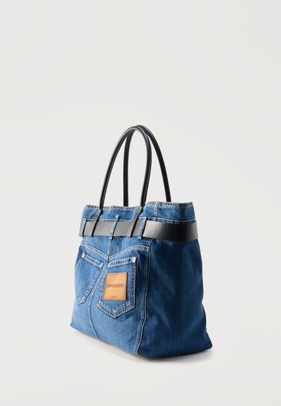 Sac cabas en denim bleu avec poignées noires, doté de poches arrière style jean et d'un patch de marque en cuir marron.