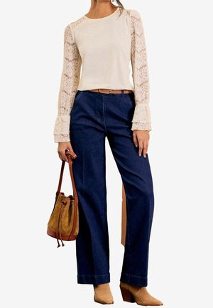Woman wearing cream lace long-sleeve blouse, dark blue high-waist wide-leg pants, tan ankle boots, and holding a brown suede bucket bag.