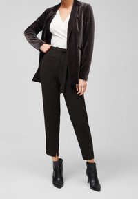 Sammetskavaj i mörkgrått, kombinerad med en vit insvept topp och svarta skräddarsydda byxor. Svarta ankelstövlar fulländar outfitten.