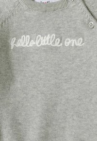 Svjetlosiva pletena džemper s okruglim izrezom, s bijelim刺7monogramom koji glasi "hello little one" i dugmadi na ramenu.