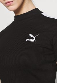 Melns ribots augstais kakls tops ar īsām piedurknēm, baltu Puma logo uz krūtīm un baltām akcentiem plecu šuvēs.