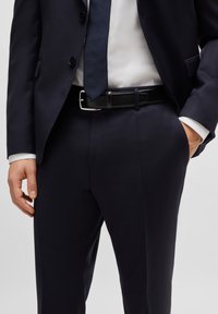 Jūrininkų kostiumas su siauru siluetu, pagamintas iš lygios medžiagos, turintis aštrų atvartą ir subtilias kišenes. Derinamas su tekstūruota kaklaraiščiu ir juodu diržu.