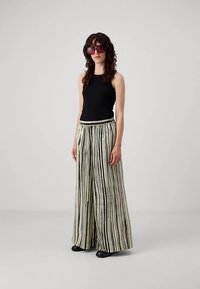 Musta hihaton paita yhdistettynä leveälahkeisiin, kerma- ja mustaraitaisiin housuihin. Housuissa on teksturoitu vyötärönauha. Mustat kengät ja aurinkolasit.