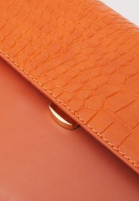 Orange struktureret læderclutch med en glat base, der har en metallisk spænde og et distinkt reptilmønster på forsiden af klappen.