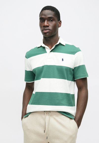 Πράσινο και λευκό ριγέ πουκάμισο πόλο με γιακά και κοντά μανίκια, που παρουσιάζει ένα μικρό λογότυπο στο στήθος. Συνδυάζεται με μπεζ παντελόνι με ελαστική μέση.