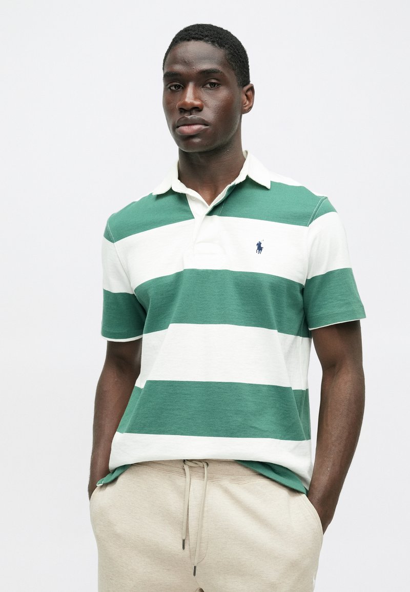 Groen en wit gestreepte polo met een kraag en korte mouwen, voorzien van een klein logo op de borst. Gecombineerd met beige elastische taillebroek.