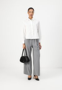 Camicia bianca con righe verticali, pantaloni grigi a gamba larga, borsa nera e scarpe con tacco nere. Design minimalista e contemporaneo.