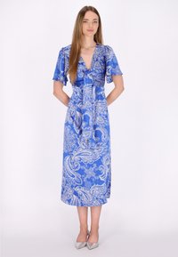 Robe bleue à motif cachemire, avec des manches courtes, un col en V et une taille cintrée. Fabriquée en tissu lisse, de longueur genoux. Des talons argentés complètent le look.