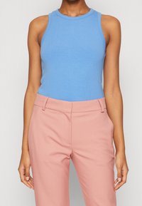 Ljust blå ribbad ärmlös topp tillsammans med rosa skräddarsydda byxor. Toppen har en rund halsringning och en åtsittande silhuett.