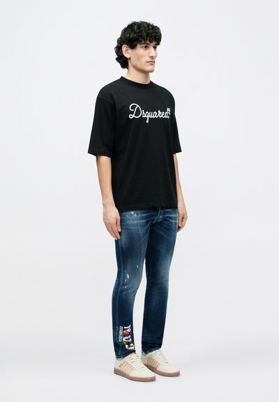 Black short-sleeve T-shirt with white logo, blue distressed jeans featuring colorful embroidered details, and white sneakers with tan accents.