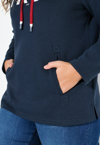 Donkerblauwe sweatshirt met rode accentkoorden, zijzakken met gestikte sluitingen en een relaxte pasvorm. Zachte, gestructureerde stof.