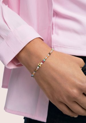 Pulsera de cuentas con piedras multicolores en tonos pastel, con un detalle en forma de letra "P" dorada. Se lleva en la muñeca sobre una camisa rosa claro.