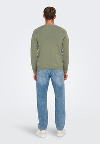Maglione verde lavorato a maglia con texture a coste, abbinato a jeans in denim azzurro chiaro. Design casual, con una vestibilità comoda e dettagli semplici.