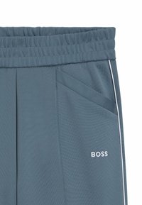 Gray athletic pants with a ribbed waistband, white accents, and a small embroidered "BOSS" logo. Features diagonal front pockets.