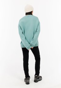 Mätovo zelený sveter so voľným strihom, s rebrovanými manžetami a lemom. V kombinácii s čiernymi nohavicami a šedými turistickými topánkami. Na hlave biely pletený čiapka.