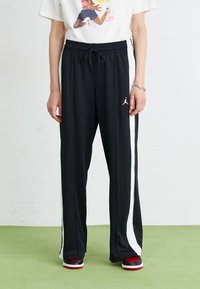 Pantalons de sport noirs avec des bandes latérales blanches, taille élastique et logo Jumpman. Le matériau semble léger et lisse.