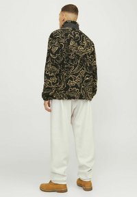 Sort og tan paisley-mønstret fleecejakke med høj krave, parret med hvide sweatpants og brune støvler. Struktureret, afslappet pasform.