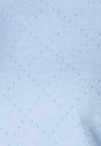 Lichtblauwe stof met een gestructureerd patroon van verheven stippen. Materiaal lijkt zacht en licht rekbaar, geschikt voor casual kleding.