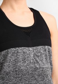 Top sportivo nero e grigio con una sezione superiore testurizzata, una sezione inferiore liscia e un dettaglio in mesh con taglio nel colletto.