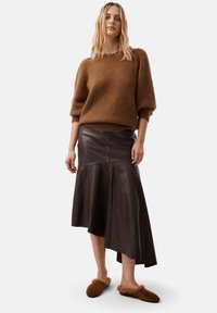 Brauner, flauschiger Pullover mit lockerer Passform, kombiniert mit einem dunkelbraunen, ledernen, asymmetrischen Rock und braunen, mit Fell gefütterten Slippern.