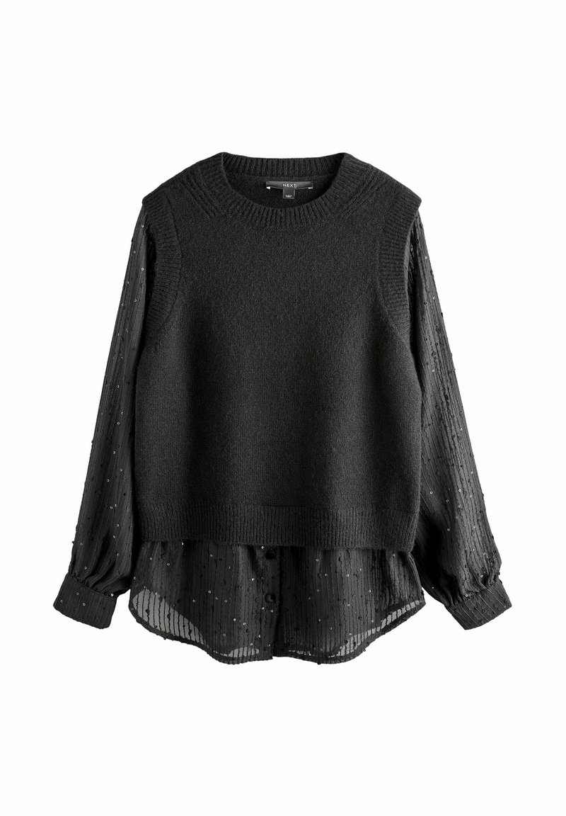 Pull en maille noire sans manches superposé à une blouse noire en voile transparent avec des rayures verticales et de petits sequins.