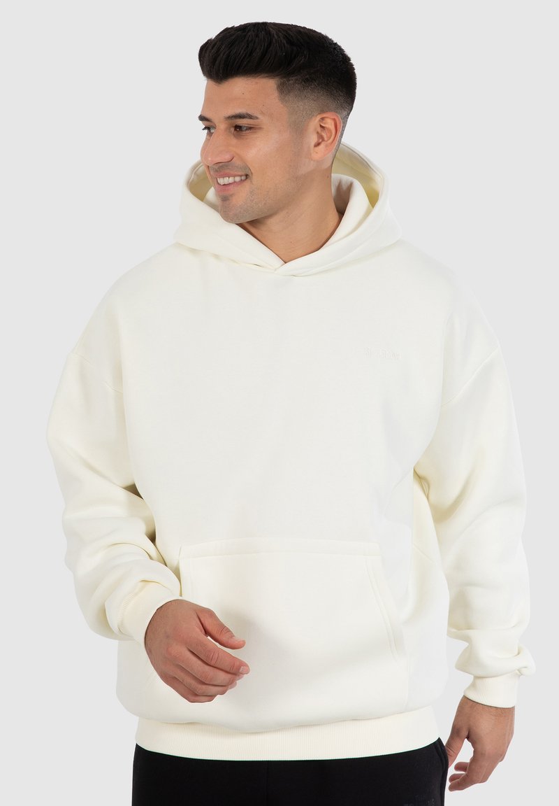 Cremefarbener Hoodie aus weichem Stoff, mit einer Fronttasche, gerippten Manschetten und einer Kordelzugkapuze. Glatte Textur, lässige Passform.