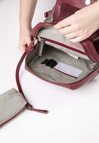Burgunderfarbene Lederhandtasche mit gestreiftem Innenfutter. Verfügt über einen Reißverschluss, ein Fach für Karten und eine abnehmbare kleine Tasche mit Reißverschluss.