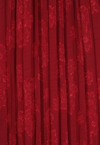 Tessuto rosso con un motivo floreale in rilievo. La texture è liscia con una leggera lucentezza e un design plissettato.