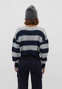 Lyhyt neulepusero, jossa on laivastonsinisiä ja harmaita vaakaraitoja, leveät hihat ja teksturoitu pinta. Yhdistetty laivastonsinisiin cargo-housuihin.