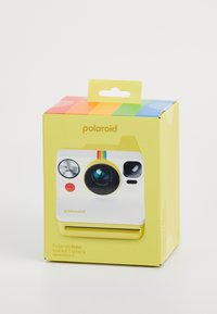 Yellow packaging for Polaroid Now Instant Camera, featuring a white camera illustration, colorful stripes on top, and prominent lens and buttons.
