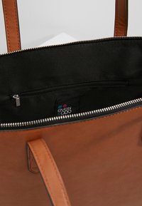 Brązowa skórzana torba tote z czarnym wykończeniem. Posiada kieszeń na zamek wewnątrz i dwa mocne uchwyty. Teksturowana powierzchnia z gładkim wykończeniem.
