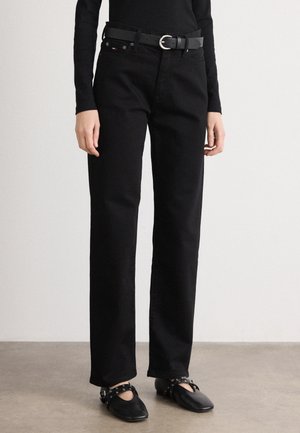 Personne portant un pantalon noir droit avec une ceinture noire, un haut noir à manches longues et des chaussures plates noires avec des brides et des œillets métalliques.