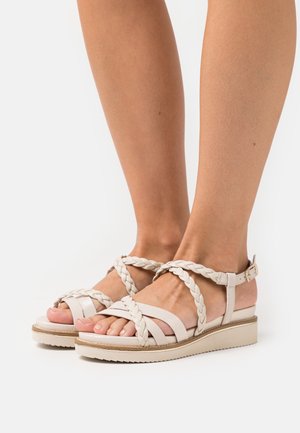 Sandales à talon compensé en cuir beige clair, avec une semelle plate et une bride de cheville réglable. Détails en cuir lisse.